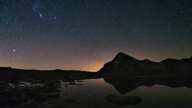 表观旋转的银河和满天星斗的天空，白雪皑皑的山山脊那边反映田园木条的湖面上。时间间隔 4 k 视频.