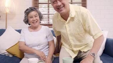 一对亚洲<strong>老夫妻</strong>在家里客厅的沙发上与孙子孙女举行智能手机视频会议。享受时间生活的<strong>老</strong>年人家庭在家里的概念。镜头前的肖像.