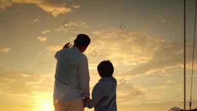 在日落的时候，父亲和儿子在游艇上挥手致意。亚洲家庭关系
