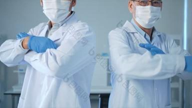 两名戴口罩的亚洲男性医生交叉着双臂，在实验室试管中看着摄像机检测蓝色液体。医疗科学保健概念