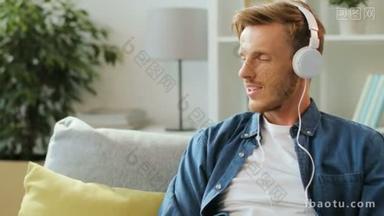 年轻时尚男子听音乐在大白色耳机上的智能手机, 而坐在沙发上, 在家里的白色背景.