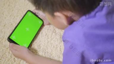 亚洲男孩学前班带着小玩艺儿在家里的手机上玩电子游戏使用和<strong>手持</strong>智能手机绿色屏幕的小孩