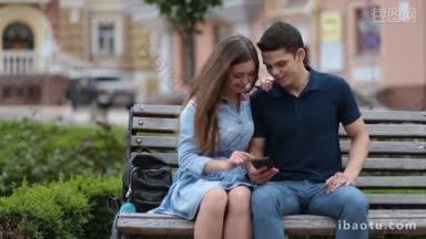 迷人的年轻情侣，悠闲地坐在公园的长椅上，浪漫的时候一起用智能手机上网