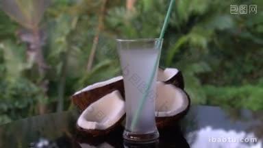 特写的椰子和椰子水与稻草在<strong>黑色</strong>玻璃桌上隔离模糊的棕榈树背景