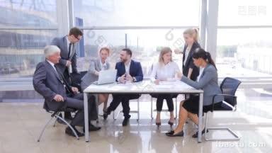 业务团队坐在桌子旁边，笔记本电脑和文件在办公室