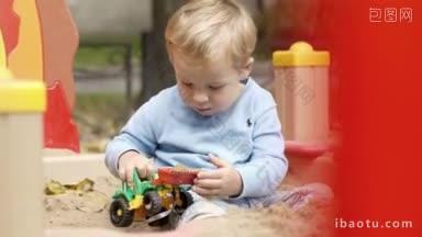 小男孩在操场上玩玩具拖拉机，他用他的玩具拿沙子，然后清空它