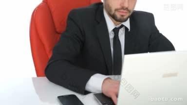 勤奋的商人坐在他的办公桌上，在他的笔记本电脑上工作，皱着眉头在键盘上输入信息