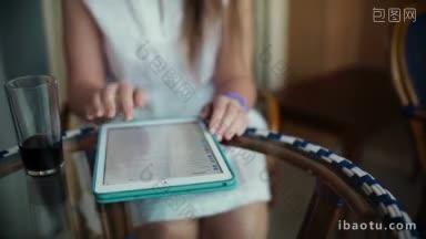 倾斜镜头的一个女人坐在酒店阳台<strong>上</strong>的<strong>桌子上</strong>，她使用平板电脑