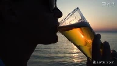 日落时分，戴墨镜的年轻女子在海滩上<strong>喝啤酒</strong>的特写镜头