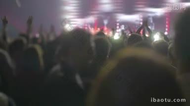 在摇滚或流行音乐演唱会上，观众在展示歌手的彩色舞台前<strong>鼓掌</strong>