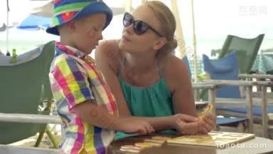 妈妈和儿子坐在海滩<strong>上</strong>的<strong>桌子</strong>旁玩游戏，妈妈帮助孩子学习数字