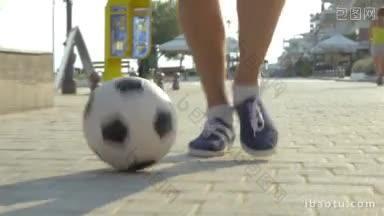 斯坦尼康的特写镜头，男子盘带足球在铺平的人行道上，在度假小镇街道，咖啡馆和酒店