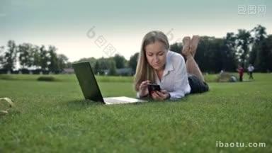 微笑着的女商人<strong>赤脚</strong>躺在公园的草坪上，用手机打字，在户外执行工作