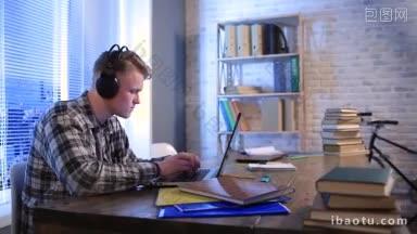 专注的学生戴着耳机在电脑上<strong>打字</strong>，坐在家里的桌子前，英俊的潮人自由职业者用笔记本电脑工作