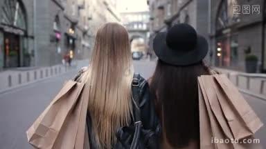 后视图两个迷人的少女购物袋在他们的肩膀上沿着城市街道慢镜头