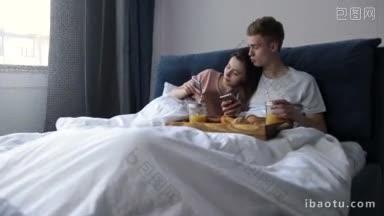 年轻的正情侣<strong>躺</strong>在<strong>床</strong>上用手机浏览社交网络，在卧室吃早餐