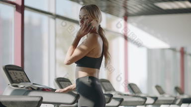 苗条的体育运动女人会说话的移动电话健身健身房适合女孩走<strong>跑步机</strong>