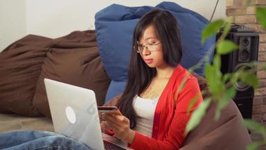 年轻的亚洲女人买在线电脑坐着豆袋椅子