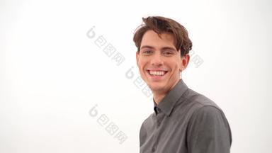 微笑英俊的年轻的男人。转修复头发相机穿灰色衬衫孤立的白色背景视频