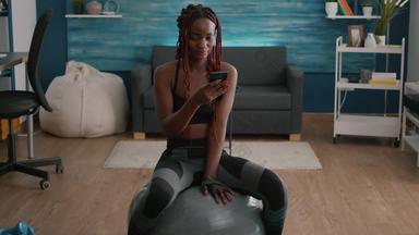 苗条的适合黑色的女人坐着健身球打字消息电话