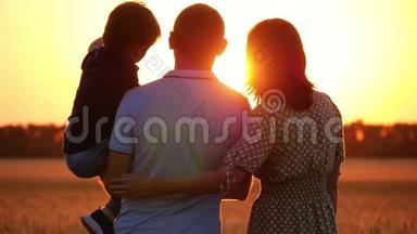 幸福的一家人看着夕阳，站在麦田里。 抱着孩子的男人.. 女人<strong>拥抱</strong>男人