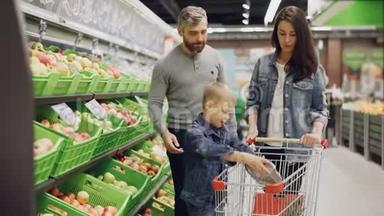 有孩子的年轻家庭正在超市买食物，父母正在挑选水果，男孩正在把它们放进超市
