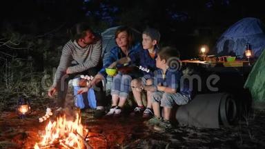 父母带着孩子在篝火上烤棉花糖到林地，幸福的家庭在大火中煎棉花糖