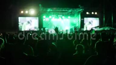 人群在摇滚音乐节上跳着舞，舞台上明亮的灯光举起扇子，兴奋的观众挥舞着手