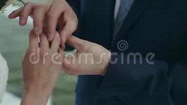 新郎把结婚戒指戴在新娘`手指上。 在水边举行婚礼。 双手合环