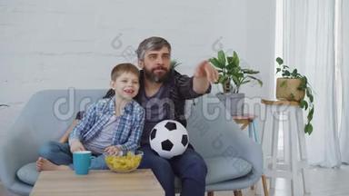 家庭成员父子俩在家里看足球比赛，欢呼庆祝胜利，吃零食