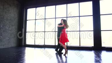 年轻夫妇跳探戈。 穿红色裙子的职业女孩和跳<strong>拉丁舞</strong>的男人。 一个现代化的工作室。