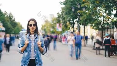 孤独的女孩游客在现代城市中站着，人们四处走动，看着镜头。 青年