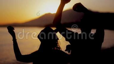 快乐的一对夫妇在海滩上跳舞，在日落时享受大自然中的蜜月。 一对夫妇一起享受浪漫的日落