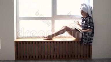 年轻女子在检疫期间呆<strong>在家</strong>里。 洗澡后坐在窗边。 看书，<strong>独自</strong>喝茶或咖啡