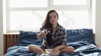 年轻女子在检疫期间呆<strong>在家</strong>里。 <strong>独自</strong>坐在床上看电视或电影。 吃爆米花，使用遥控器