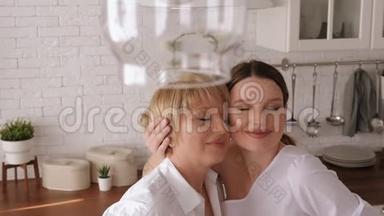 一个成年女儿在家中厨房里<strong>拥抱</strong>她年迈的母亲。