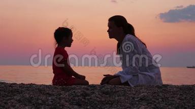 母亲在日落时在海边或海边与她的小女儿交谈。