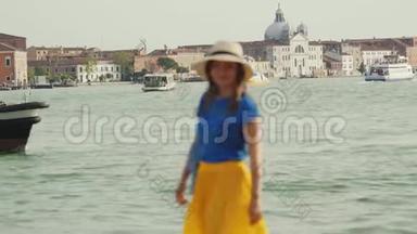 戴帽子的女士站在大运河的码头上，欣赏威尼斯的景色，转身微笑