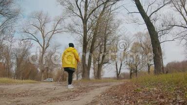 在秋天的森林里做北欧行走的高级妇女。 在秋天的小径上进行北欧步行比赛。 退休人士健康