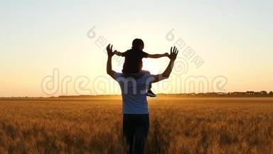 日落时父亲和孩子的剪影。 男孩举起双手在空中模仿一次美妙的日落飞行