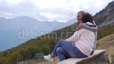 坐在木凳上的老年旅行者拥抱并欣赏山景