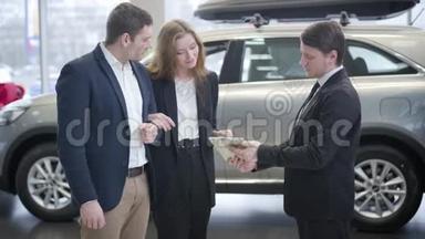 穿西装的白人和汽车经销商的年轻夫妇交谈。 成功的家庭在展厅买新车