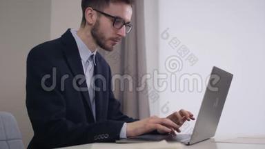 在笔记本电脑上打眼镜的英俊白人商人的侧视肖像。 年轻的聪明人