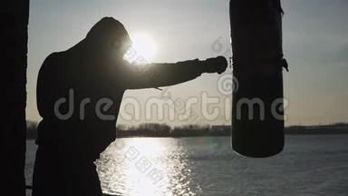 <strong>剪影</strong>。 拳击手在美丽的日落和河流上打拳击梨。 在露天锻炼。 拳击和<strong>武术</strong>