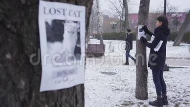 焦点变化从年轻的白种人女人在树的背景上悬挂丢失的宠物广告到在一个公告