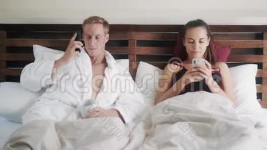 一对夫妇早上躺在床上，男人打电话，女人上网聊天