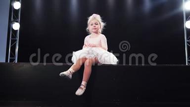 美丽的小女孩芭蕾舞演员穿着粉红色的芭蕾舞裙坐在舞台上。 孩子们`芭蕾。 慢动作