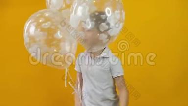 快乐的小男孩蹒跚学步，带着气球跳舞，背景是黄色的