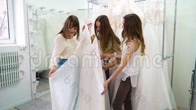 兴奋的新娘和伴娘们在婚礼沙龙里试穿时髦的白色连衣裙