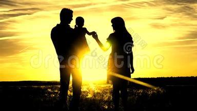 幸福家庭的剪影，在美丽的金色阳光下行走。 孩子在田里和爸爸妈妈玩。 爸爸